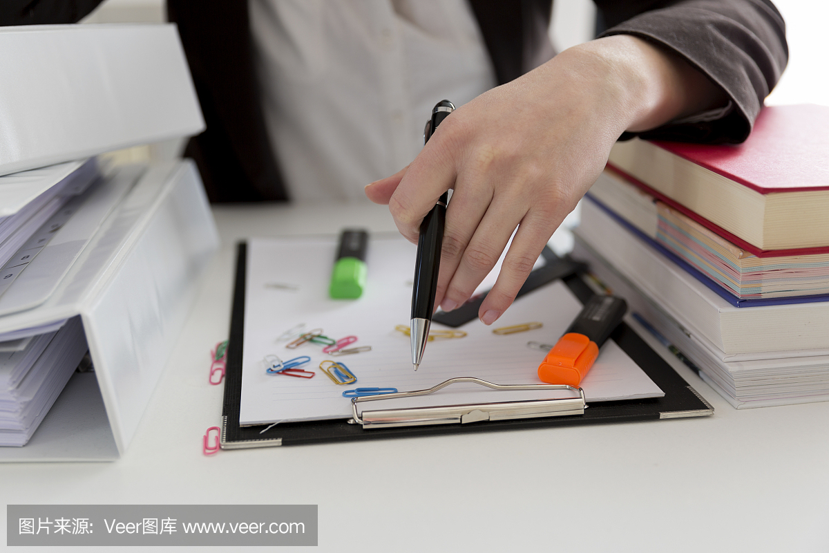 坐在滿是文書,書籍和文件的桌子旁的女人?；靵y的工作場所。過載和過度勞累